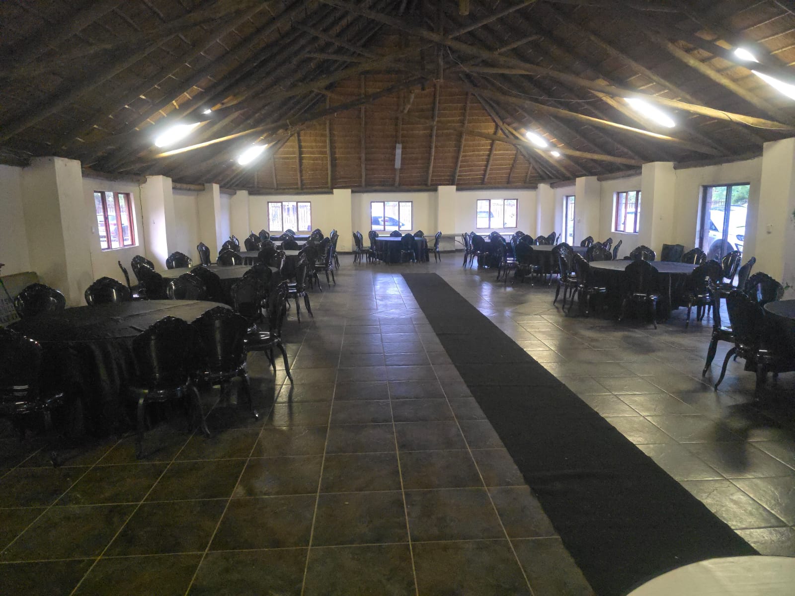 Reception hall set with round tables, black chairs and a centre aisle runner