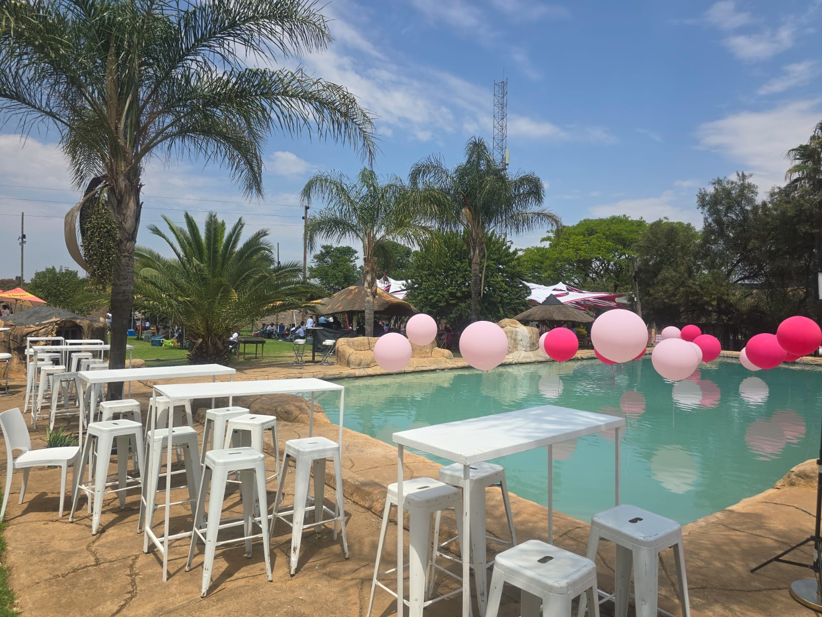 Pool decorated with pink balloons and white bar tables